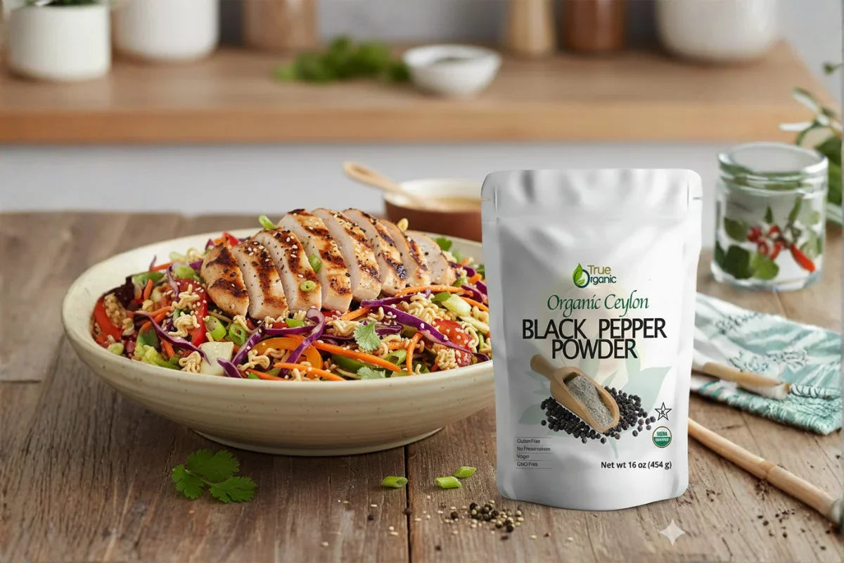 Grilled chicken salad with colorful vegetables beside a pack of Organic Ceylon Black Pepper Powder on wooden table