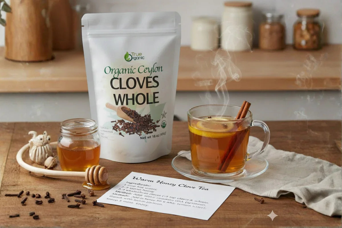 Organic Ceylon cloves whole, honey jar, and steaming warm honey clove tea with lemon and cinnamon on wooden table